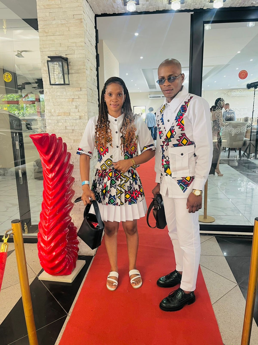 Two people posing on a red carpet in an indoor setting, fashion show, with a modern interior design.
