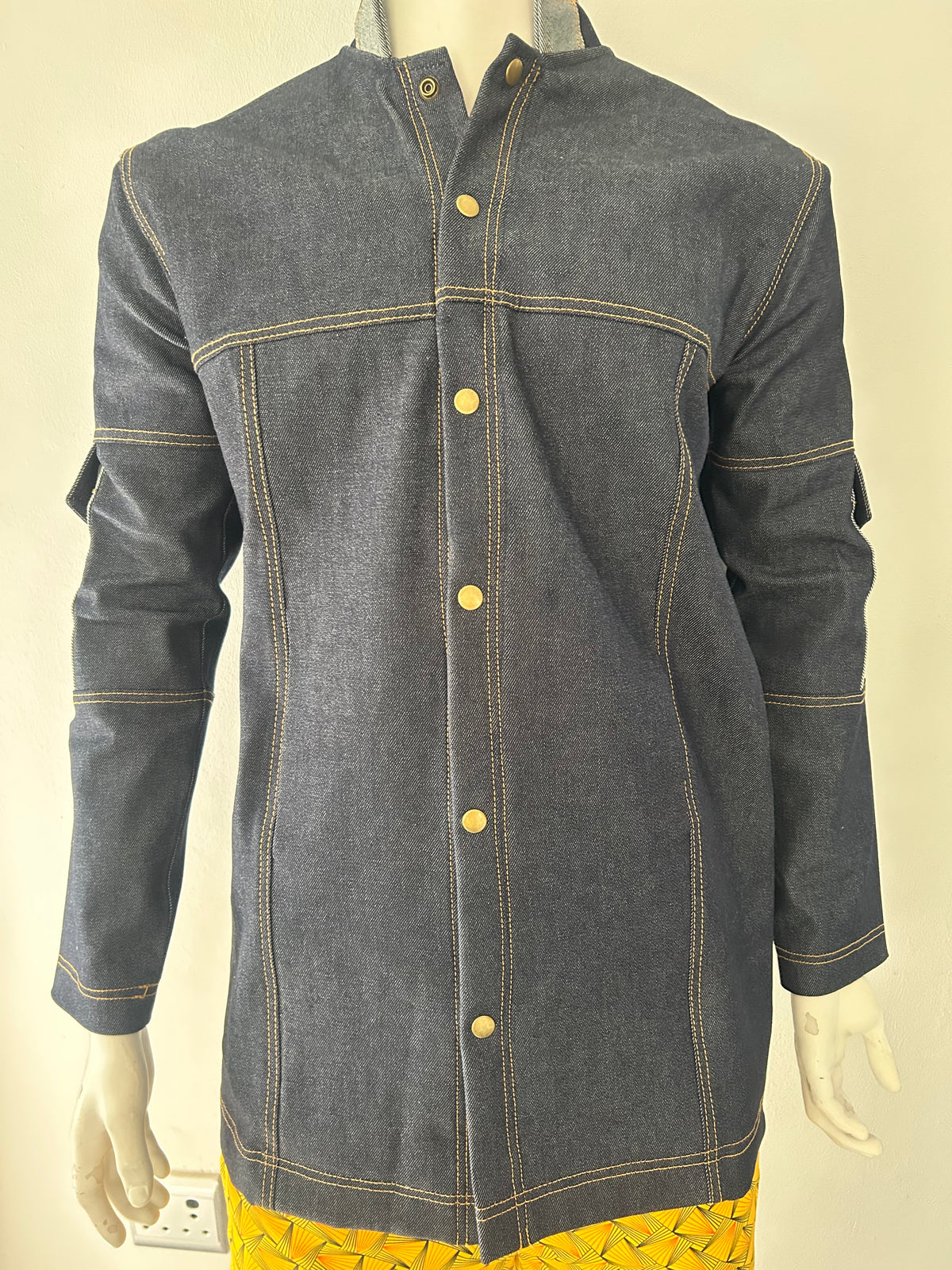Angled close-up of a dark blue denim jacket on a mannequin, showing the raised collar, contrast stitching and side pocket.