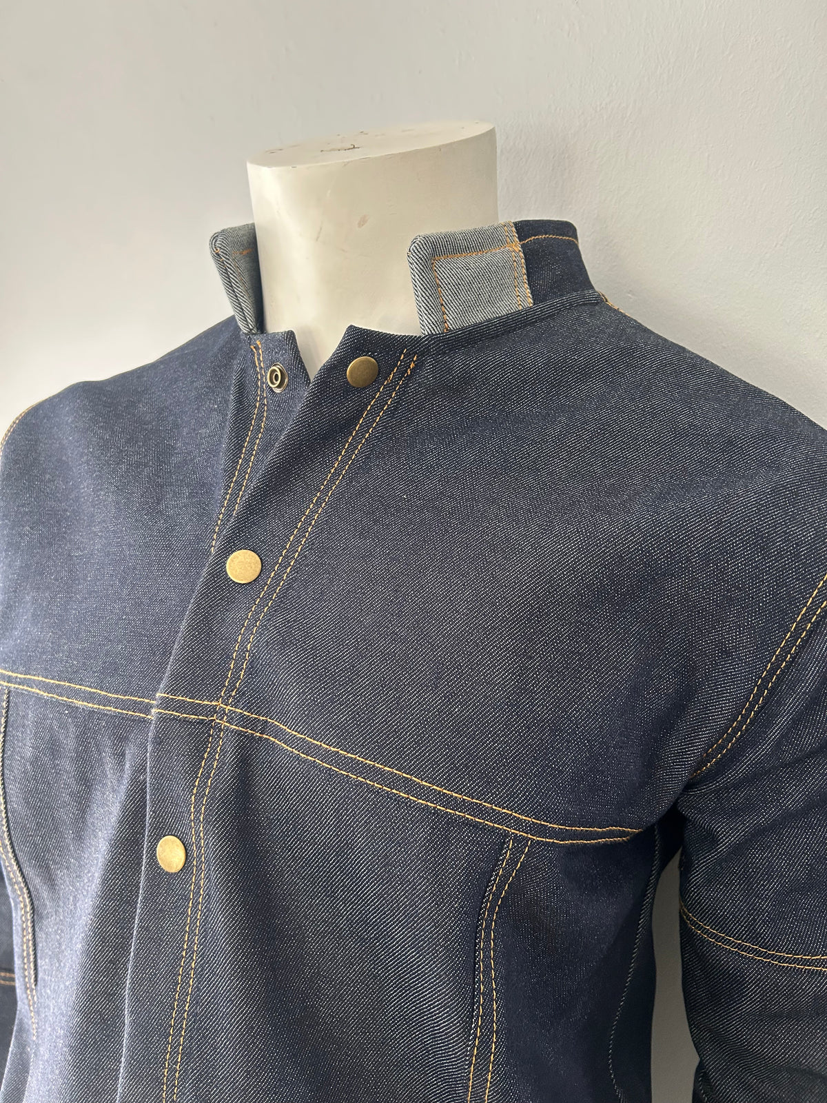 Front-side view of a dark blue denim jacket on a mannequin, showing grey back and sleeve panels with contrast stitching.