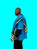 Side view of a man wearing a blue Xhosa top and draped shawl with black and yellow striped trim, styled with black trousers.