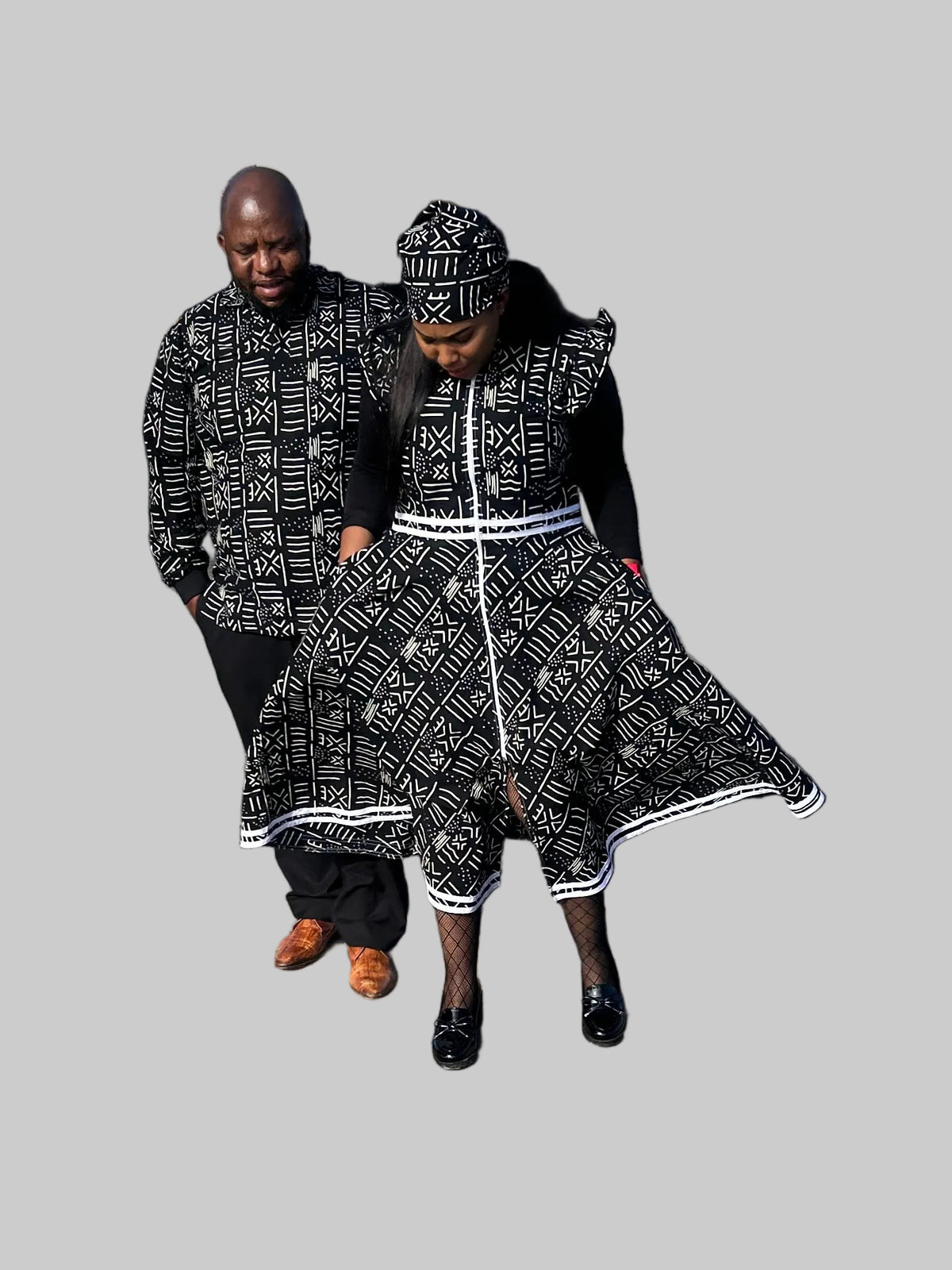 A man and a woman wearing matching black and white patterned traditional clothing walk together in a parking lot in front of a restaurant.