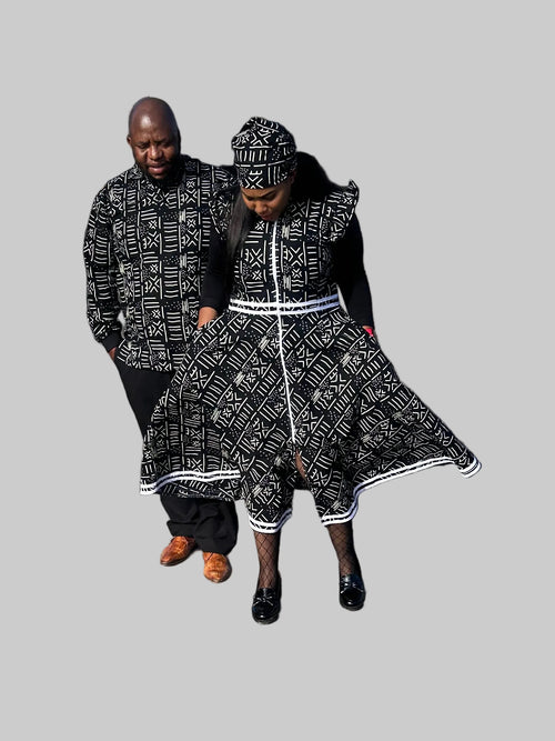 A man and a woman wearing matching black and white patterned traditional clothing walk together in a parking lot in front of a restaurant.